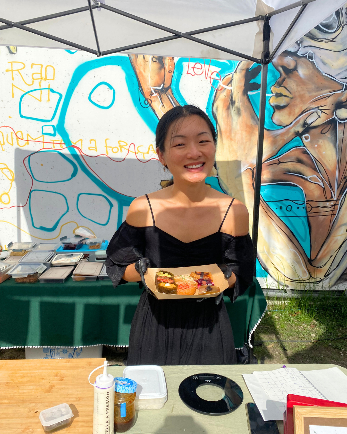 Tiny Leaf founder smiling while holding a plate of vegan Asian dishes at an outdoor market stall.