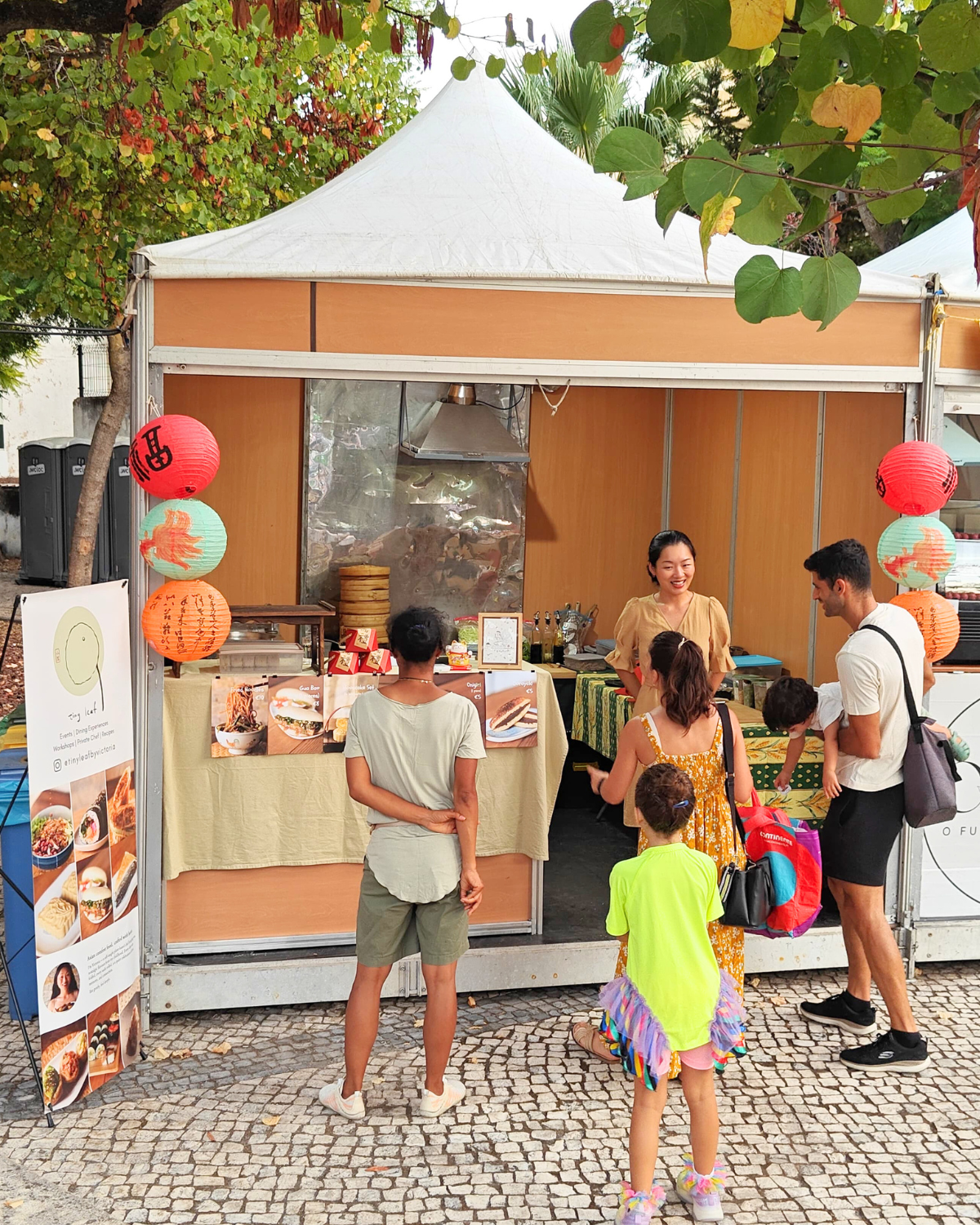 Tiny Leaf vegan Asian food stall decorated with red lanterns at an outdoor market in Portugal.