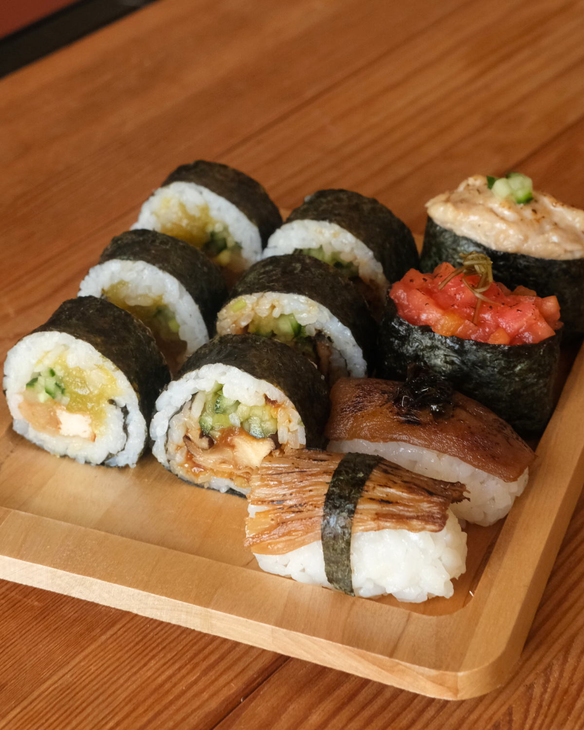 Assorted vegan sushi platter with maki rolls and nigiri served on a wooden tray.