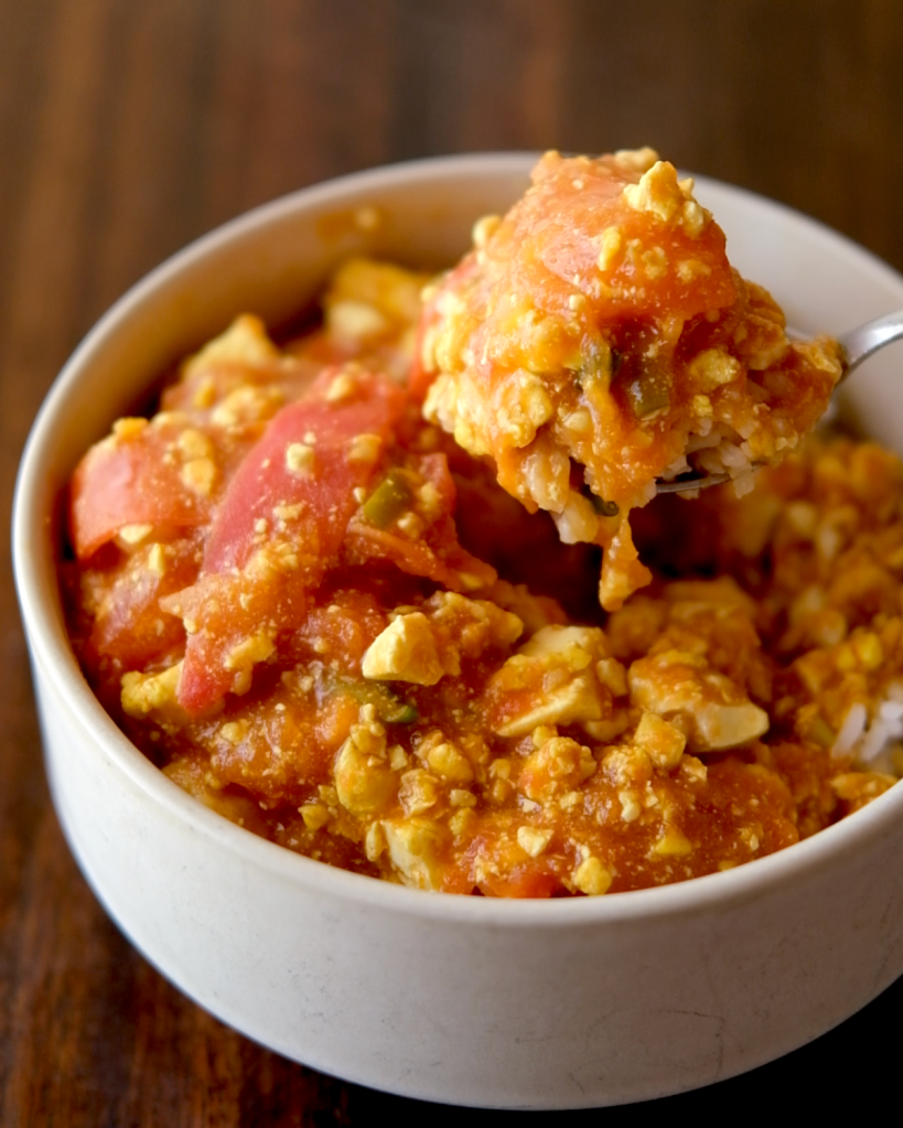 Bowl of vegan tomato scrambled eggs served over rice with tofu and scallions.
