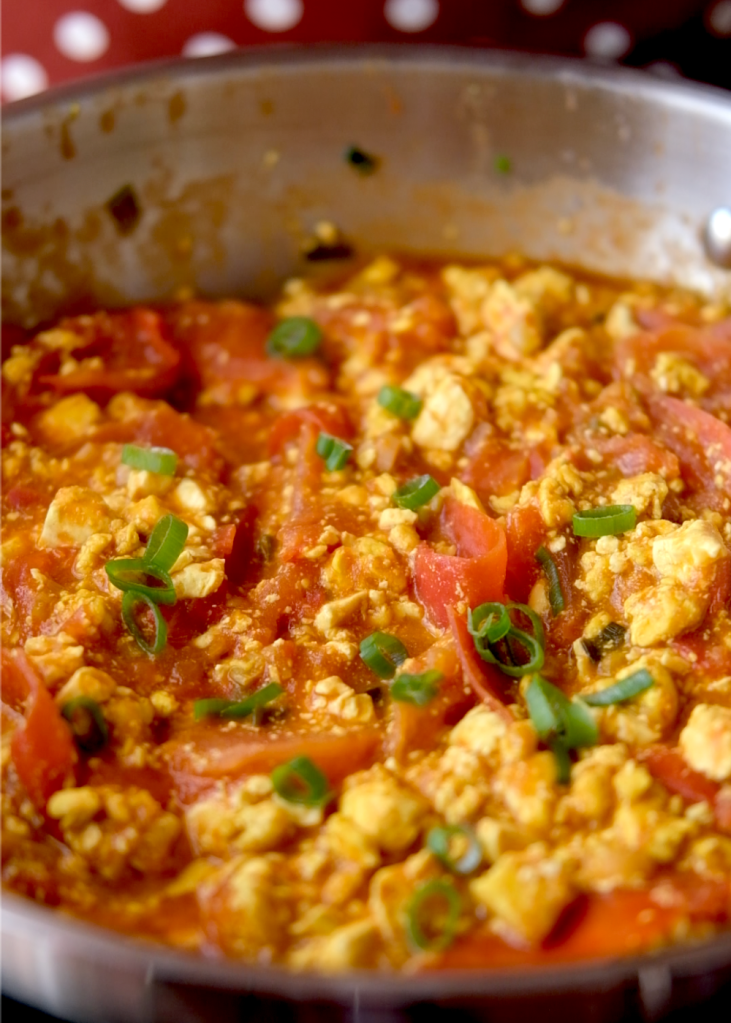 Vegan tomato scrambled eggs with tofu and fresh tomatoes cooking together in a pan.