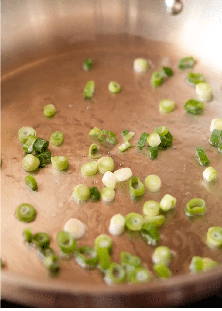 Chopped scallions sautéing in oil to build flavour for vegan tomato scrambled eggs.