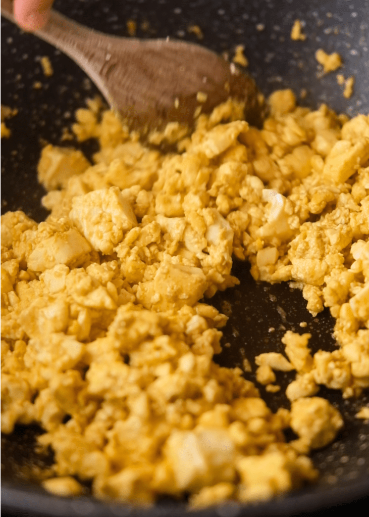 Tofu scrambled with turmeric and nutritional yeast to create an egg-like texture for vegan tomato scrambled eggs.